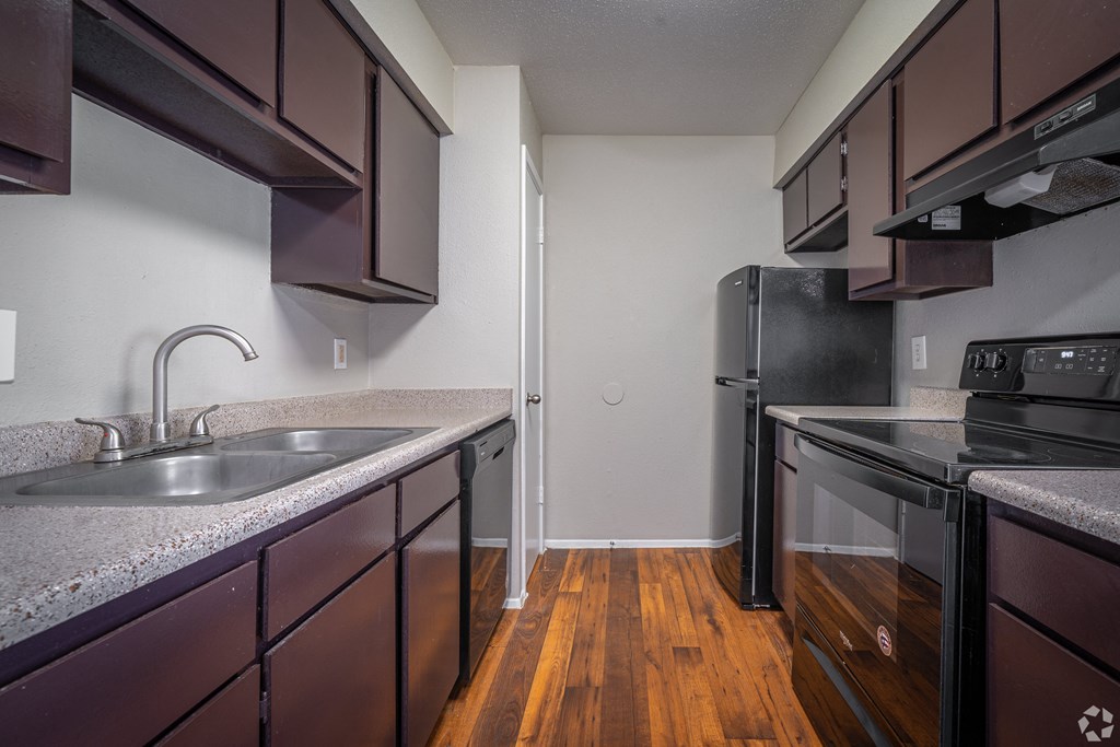 an empty kitchen with black appliances and wood flooring in an apartment