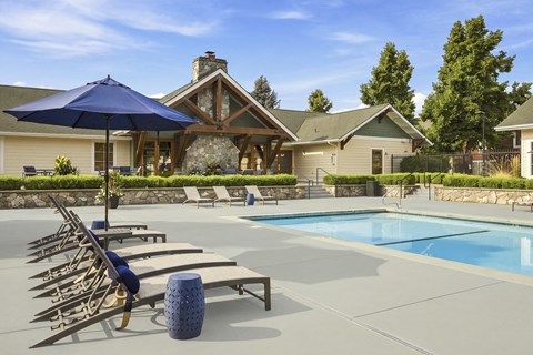 A pool with sun loungers and a blue umbrella in front of a house.