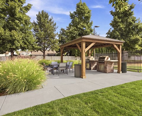 A wooden gazebo is surrounded by trees and a fence.