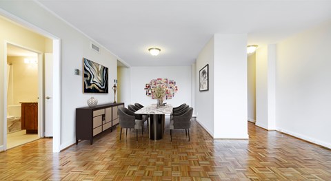 Spacious dining room with parquet floors, marble-top table, upholstered gray chairs, and colorful wall art