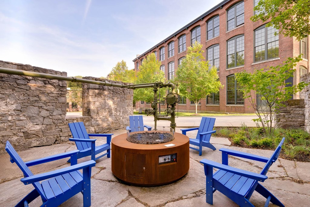 Outdoor fire pit with blue Adirondack chairs in a courtyard setting.