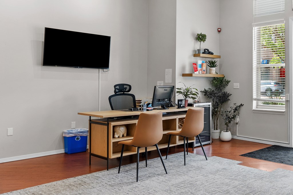 A room with a desk, chairs, and a TV mounted on the wall.