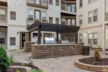 A patio with a table and chairs is surrounded by a stone wall and a garbage can.