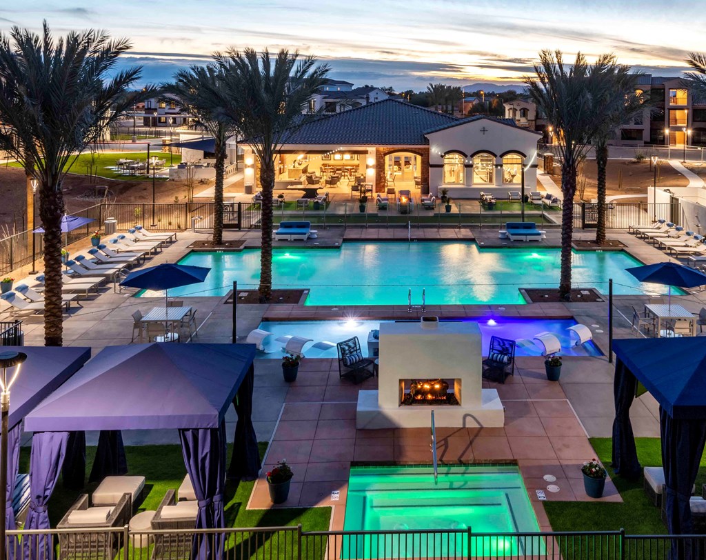 Chandler, AZ, Apartments for Rent - The Core Chandler - Gated Outdoor Resort-Style Pool Area with Swimming Pool, Hot Tub, Lounge Seating, Blue Tent Cabanas, Tables with Blue Umbrellas and Chairs, Palms Trees, and View of the Resident Clubhouse.