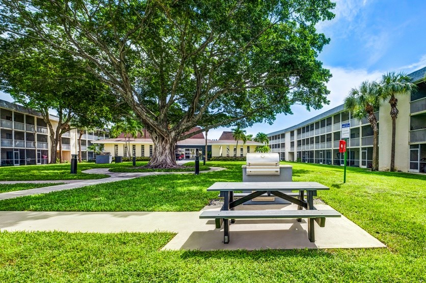 Green courtyard with picnic tables at Coronado Springs Apartments in Palm Springs, FL. Pet-friendly outdoor space for residents to relax.
