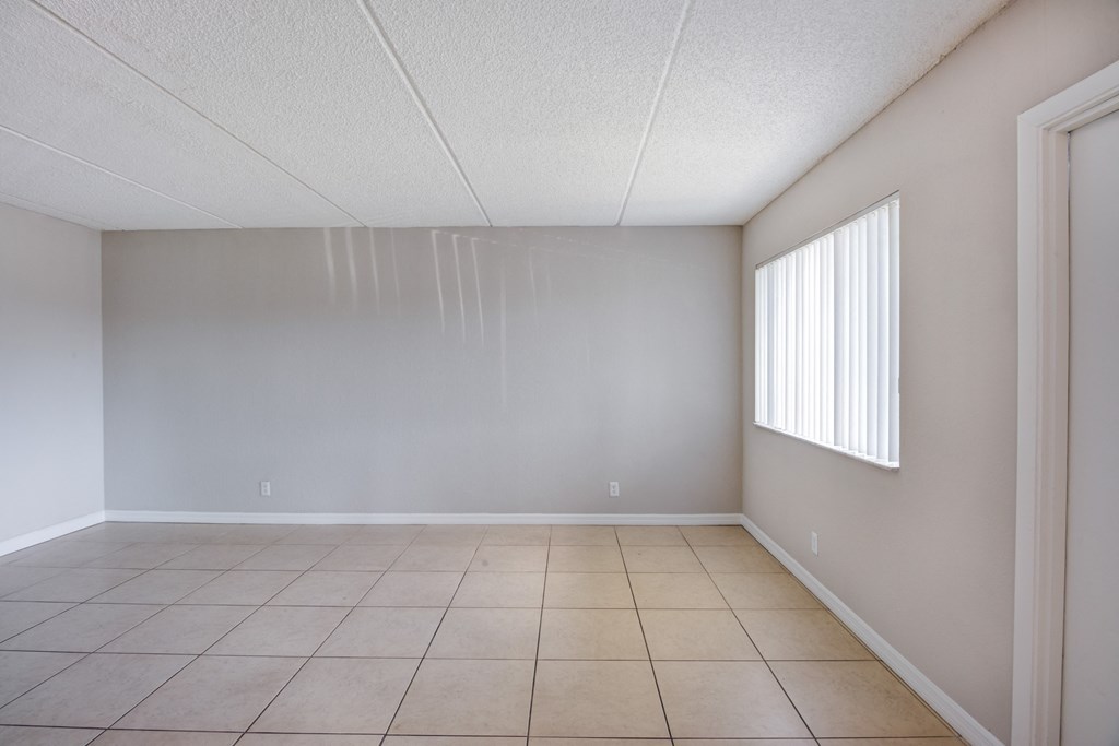 an empty living room with a window and a tiled floor
