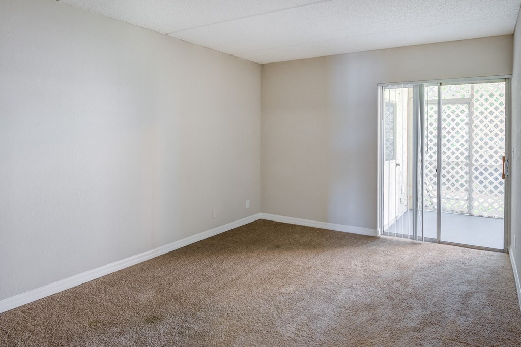an empty living room with a sliding glass door to a balcony