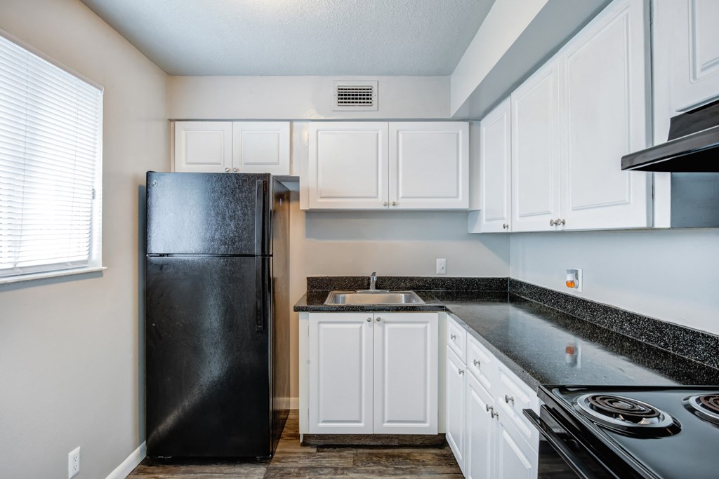 an empty kitchen with white cabinets and a black refrigerator