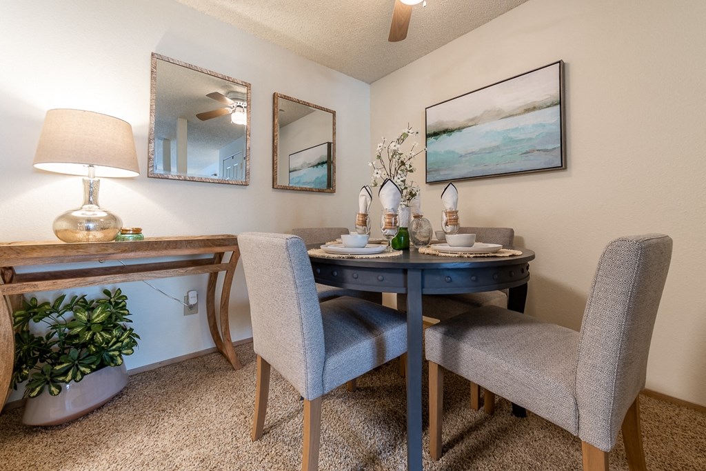 Kent, WA Apartments, With In-Unit Washer And Dryer - Country Glen - A Stylish Dining Area With A Round Table, Ceiling Fan, Large Wall Painting, Framed With Mirrors, And A Potted Green Plant.