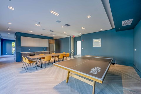 Modern recreation room with a ping pong table, long dining table, and kitchen area.