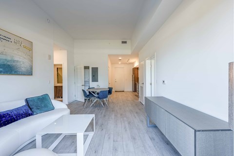 Bright, modern apartment interior with white sofa, dining table, and light wood floors.