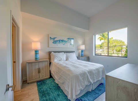 Bright bedroom with queen bed, blue rug, and palm tree view.