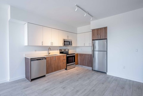 Modern kitchen with white and wood cabinets, stainless steel appliances, and light wood flooring.