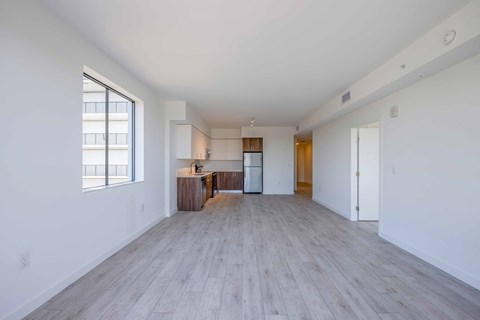 Modern apartment interior with white walls, light wood flooring, and open kitchen.