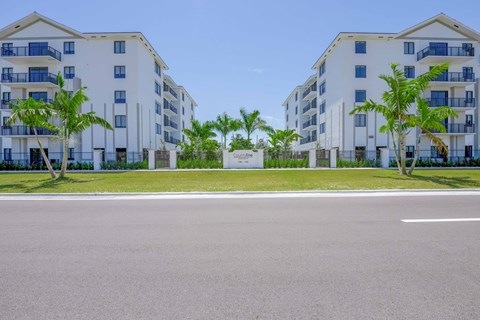 Exterior view of modern white apartment buildings with balconies and palm trees.