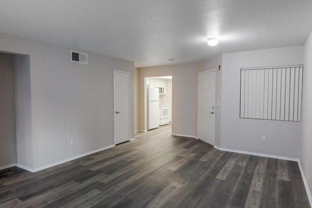 the living room and dining room of an apartment with white walls and wood flooring