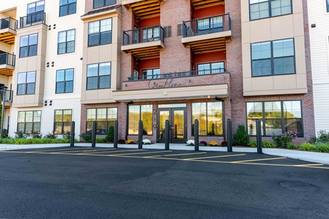 Front entrance of Creekline at Fairfield apartments in Fairfield, CT featuring a modern brick-and-siding exterior, glass entry doors, and balcony residences above.