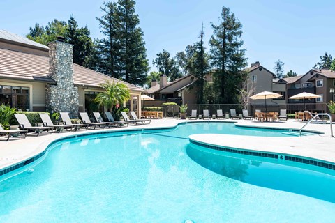 A large swimming pool with a stone pillar and a row of sun loungers.
