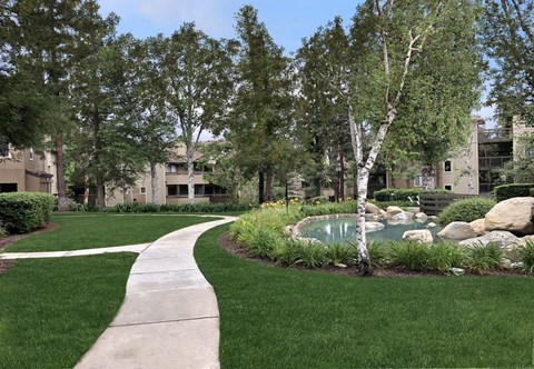 A walkway leads through a landscaped area with a pond and rocks.