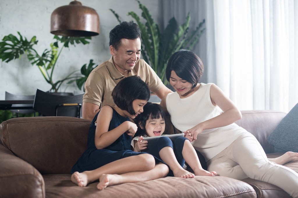 a family sits on a couch while looking at a tablet
