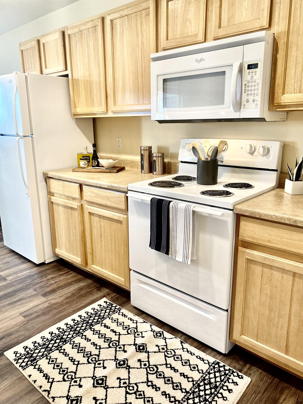 Spokane, WA Apartments for Rent - Deer Creek - Kitchen with Plank Flooring, Rug, White Appliances, and Wood-Tone Cabinetry.