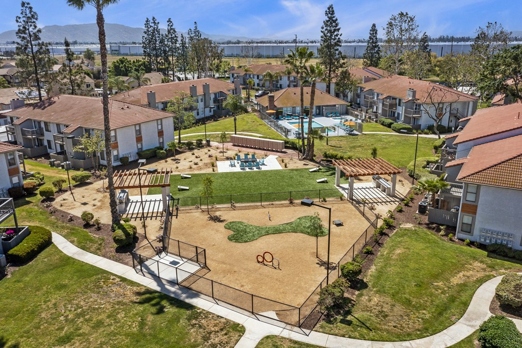 Dog-Friendly Apartments in Moreno Valley, CA - Ardella on Chagall - Aerial View of Property Grounds Showcasing Aparment Buildings, Fenced Dog Park, BBQ Area with Grilling Stations, Cornhole Playing Field, and Pool Area.