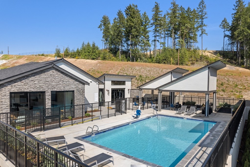 a swimming pool with lounge chairs around it and a building with a grassy hill in the background,