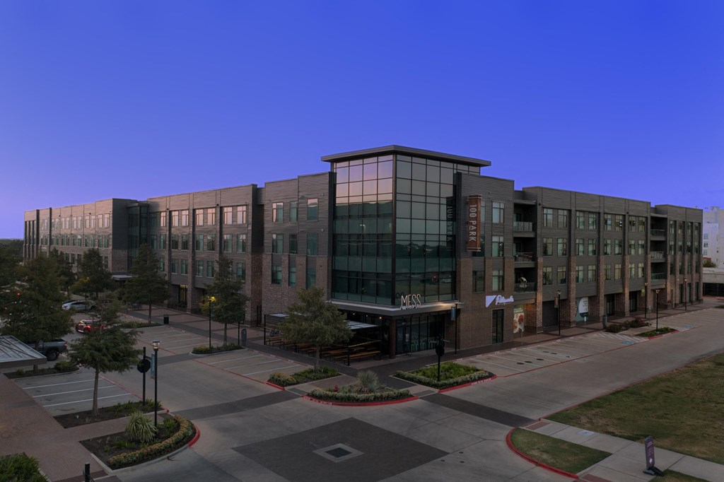 A large modern building with glass windows and a parking lot in front.