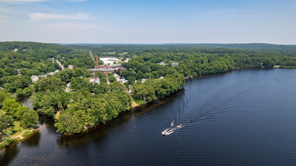 Aerial view of a lake with a boat pulling a tube near a wooded shoreline and a brick industrial building.