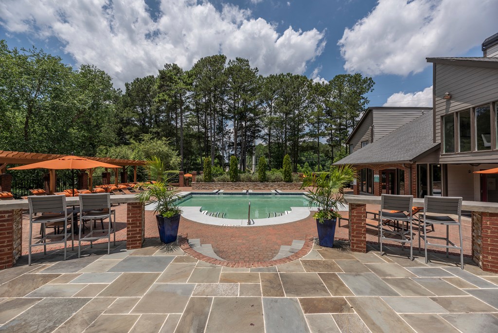 a backyard with a pool and patio with chairs and umbrellas
