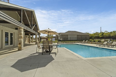 the pool and patio area of a house with chairs and umbrellas