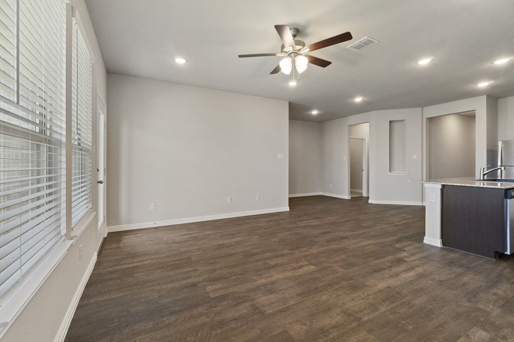 an empty living room with a ceiling fan and a kitchen