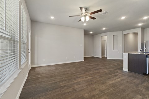 an empty living room with a ceiling fan and a kitchen