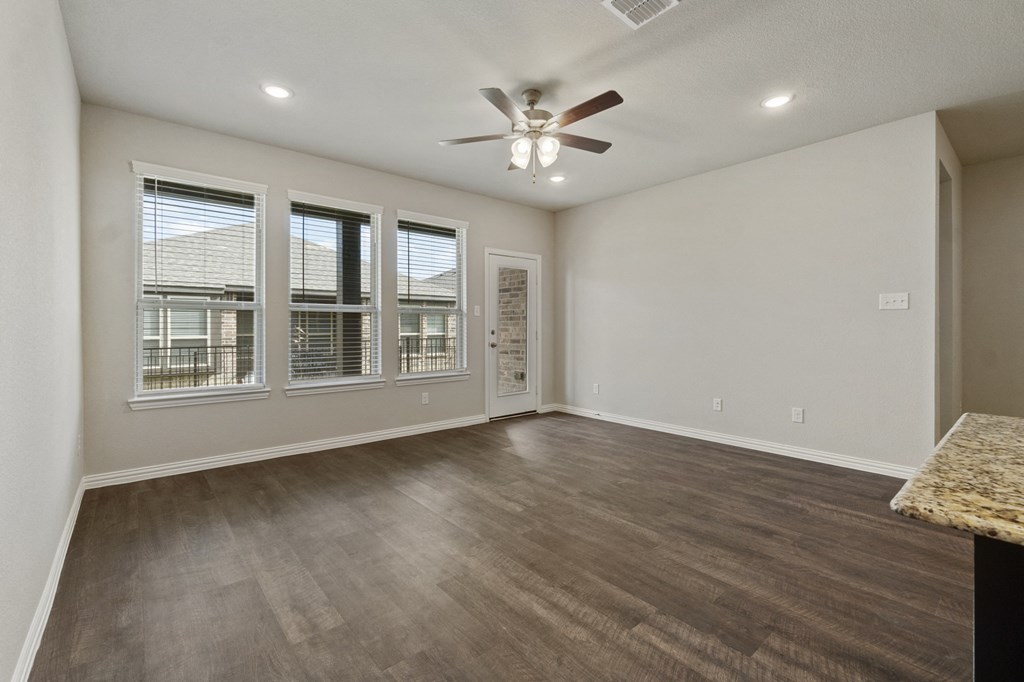 an empty living room with a ceiling fan and windows