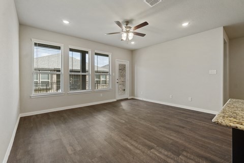 an empty living room with a ceiling fan and windows