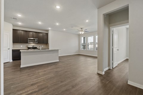 an empty living room with a kitchen and a ceiling fan