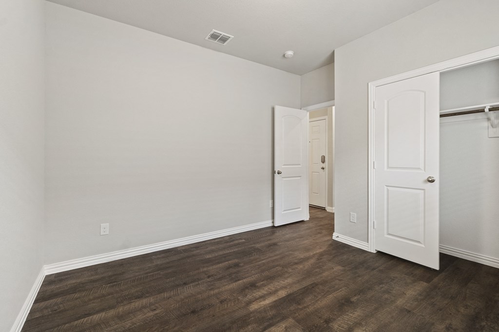 a bedroom with white walls and wood flooring and a closet
