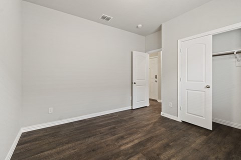 a bedroom with white walls and wood flooring and a closet