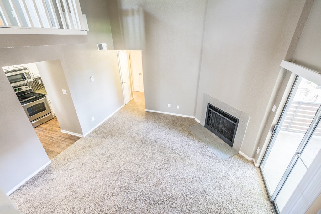 an empty living room with a fireplace and a door to a kitchen