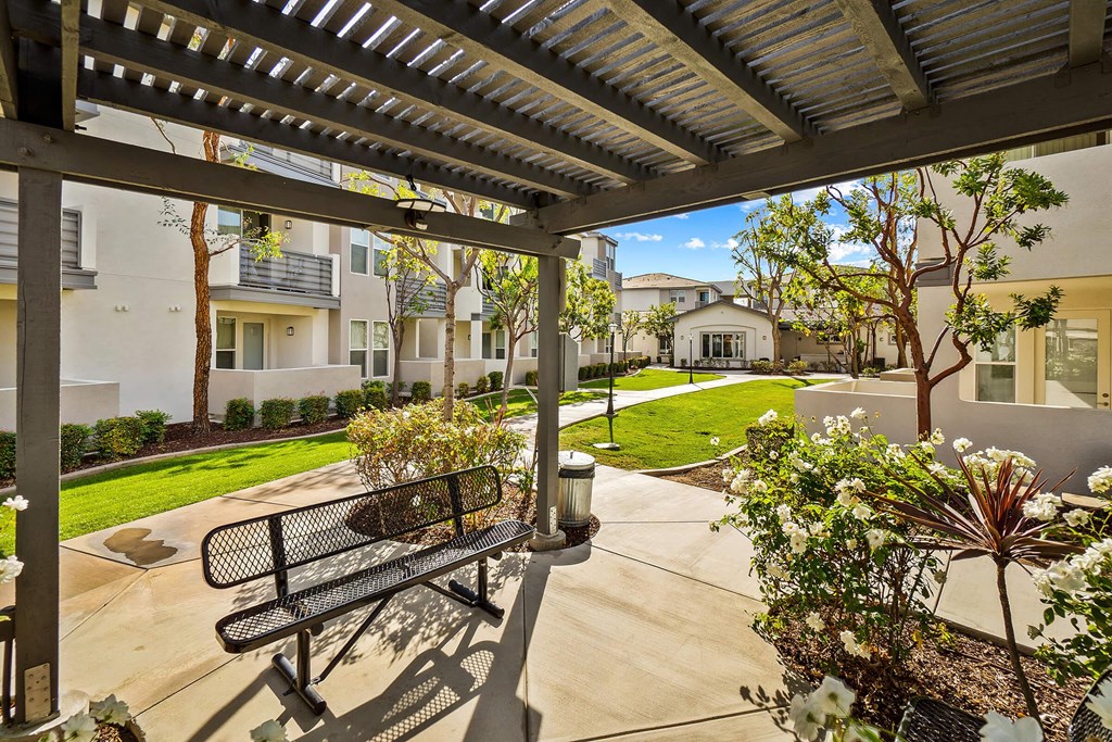 a pergola with a bench and trees in front of apartment buildings