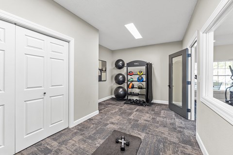 A room with a grey carpet and a black exercise ball.