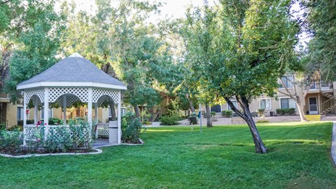 Two-Bedroom Senior Apartments in Paradise, Las Vegas, NV - Gramercy Parc Senior Apartments - Courtyard With White Gazebo, Mature Trees, Green Lawn, And Apartment Buildings Along Shaded Walkways.