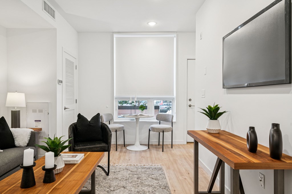 A modern living room with a grey couch, a black chair, a wooden table, and a flat-screen TV mounted on the wall.