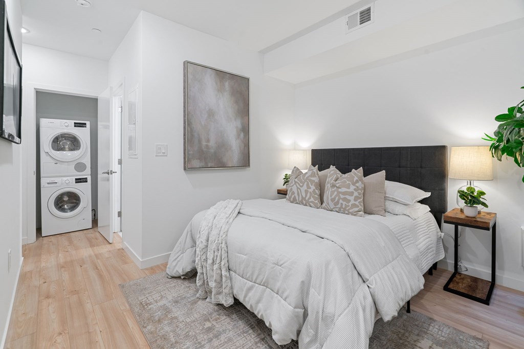 A bedroom with a large bed and a washing machine in the corner.