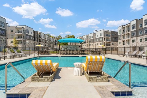 Two yellow and white striped sun loungers are on the edge of a pool.