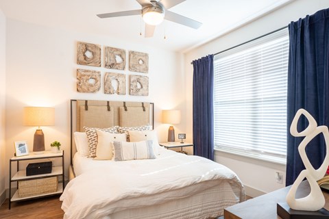 A bedroom with a large bed, a ceiling fan, and a nightstand with a lamp.
