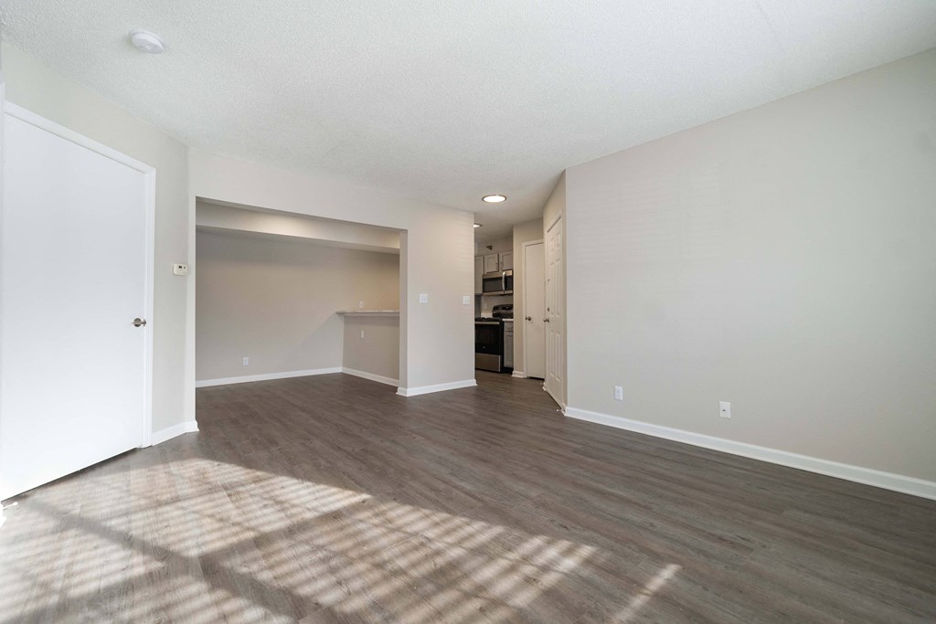an empty living room and kitchen with white walls and wood flooring