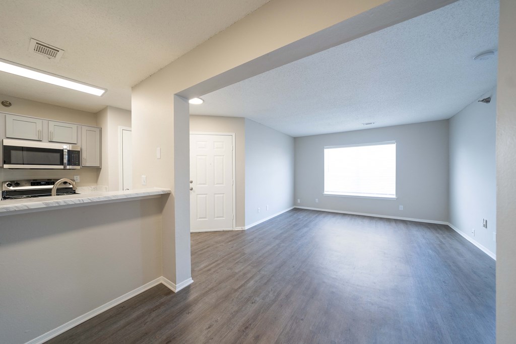 an empty living room and kitchen with hard wood flooring