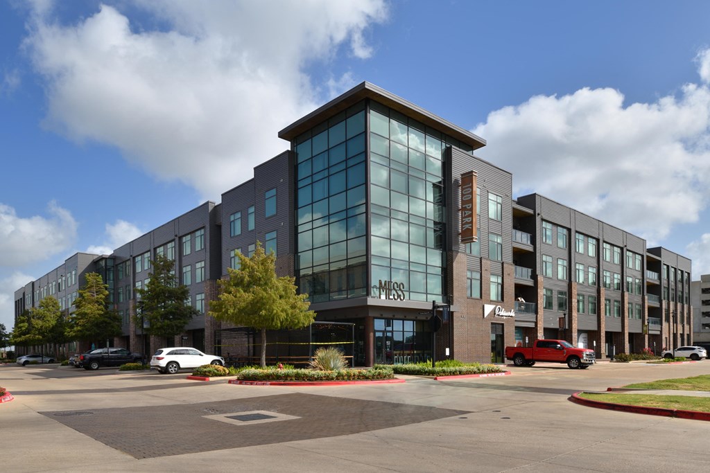 A modern building with a glass facade and a parking lot in front.