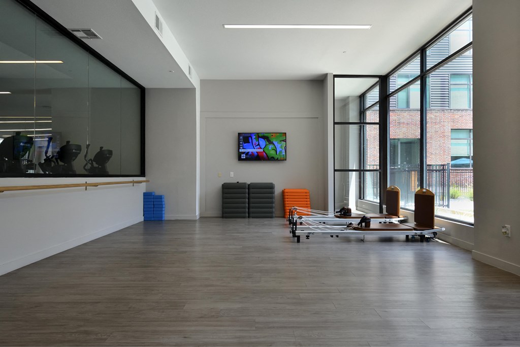 A spacious room with a TV mounted on the wall and a row of chairs in front of it.